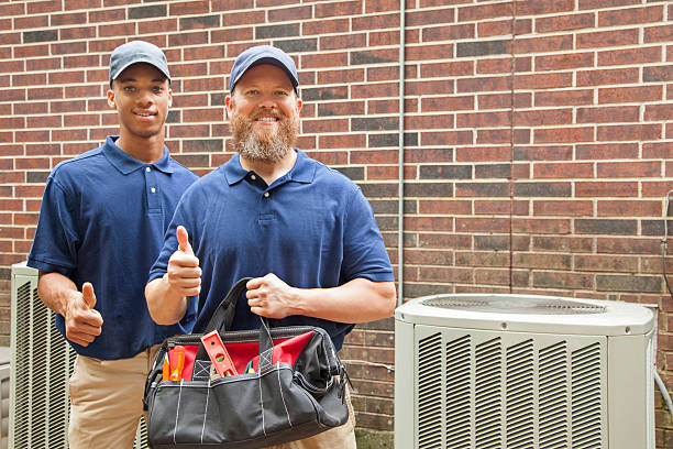 Illustrative photograph of two workers with a tool bag beside an air conditioning unit